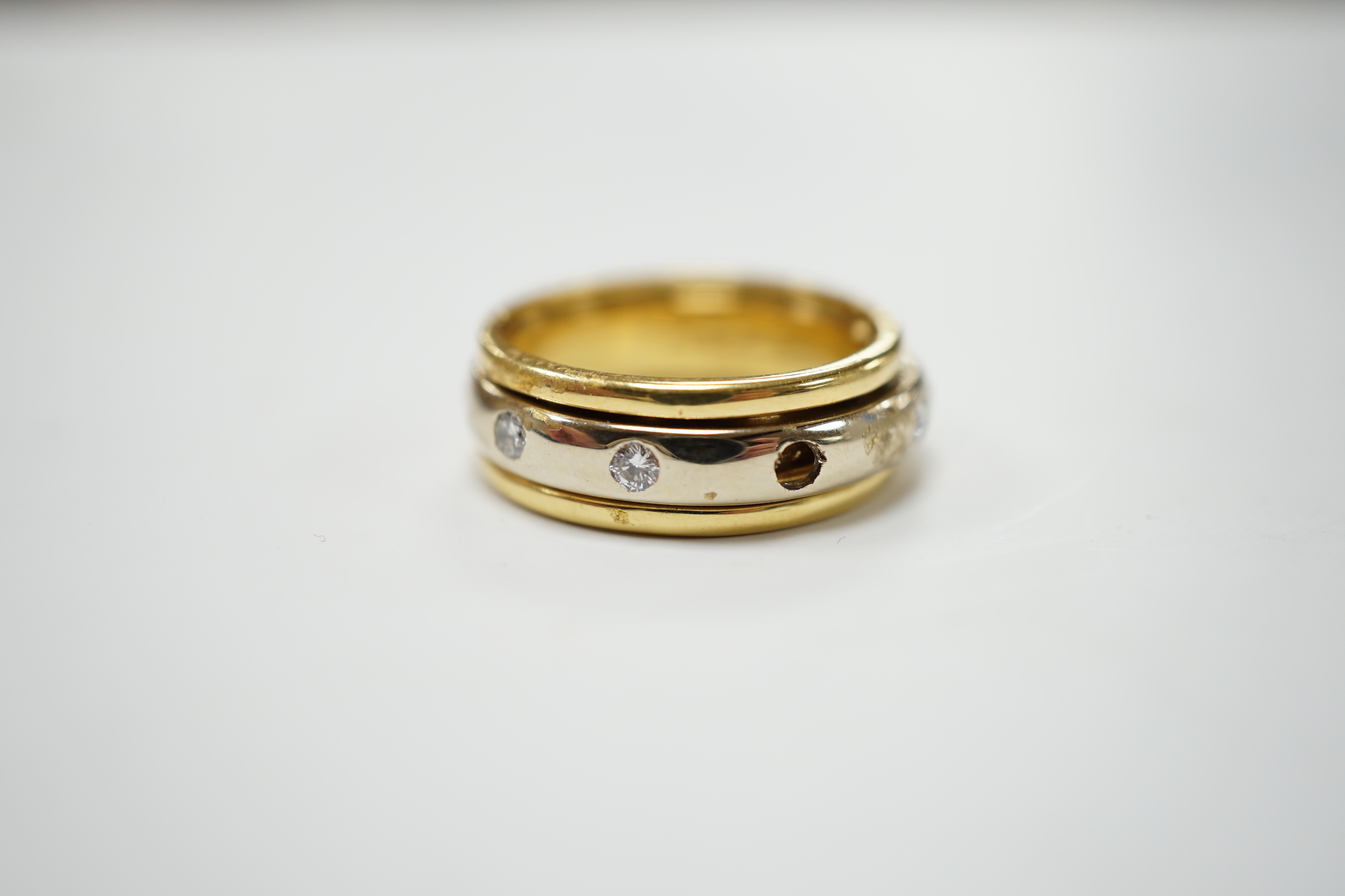 A modern 750 yellow metal ring, with central diamond set rotating white metal band (stone missing), size P/Q, gross weight 7.9 grams.